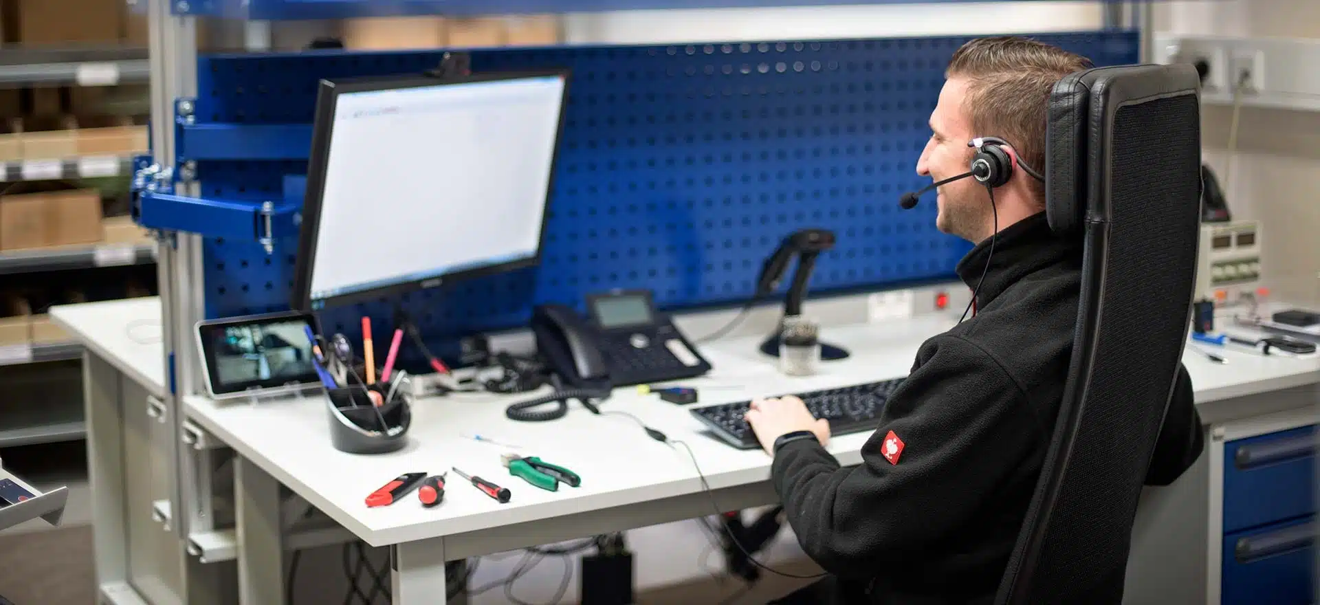 Mann mit Headset arbeitet am Computer an einem Schreibtisch in einer Werkstatt