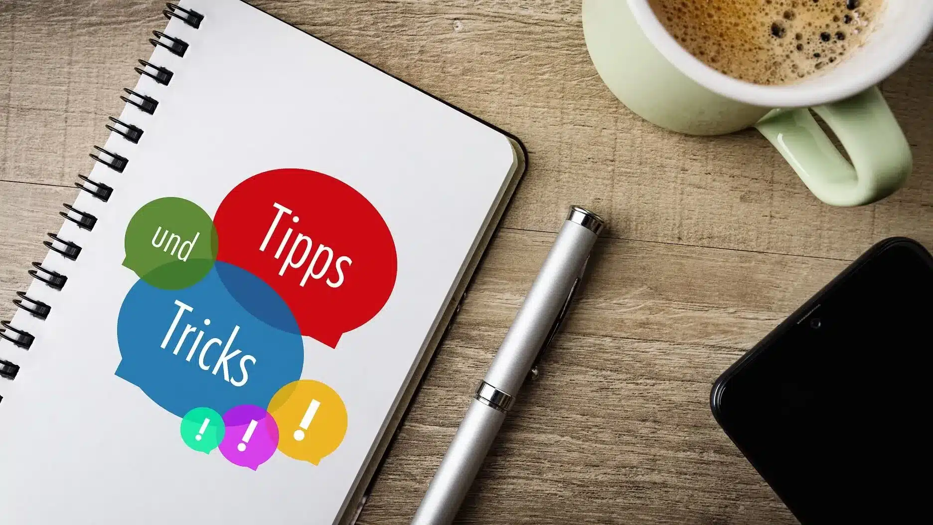 Notizbuch mit den Worten „Tipps“, „Tricks“ und „und“ auf dem Tisch neben Kaffee, Stift und Smartphone