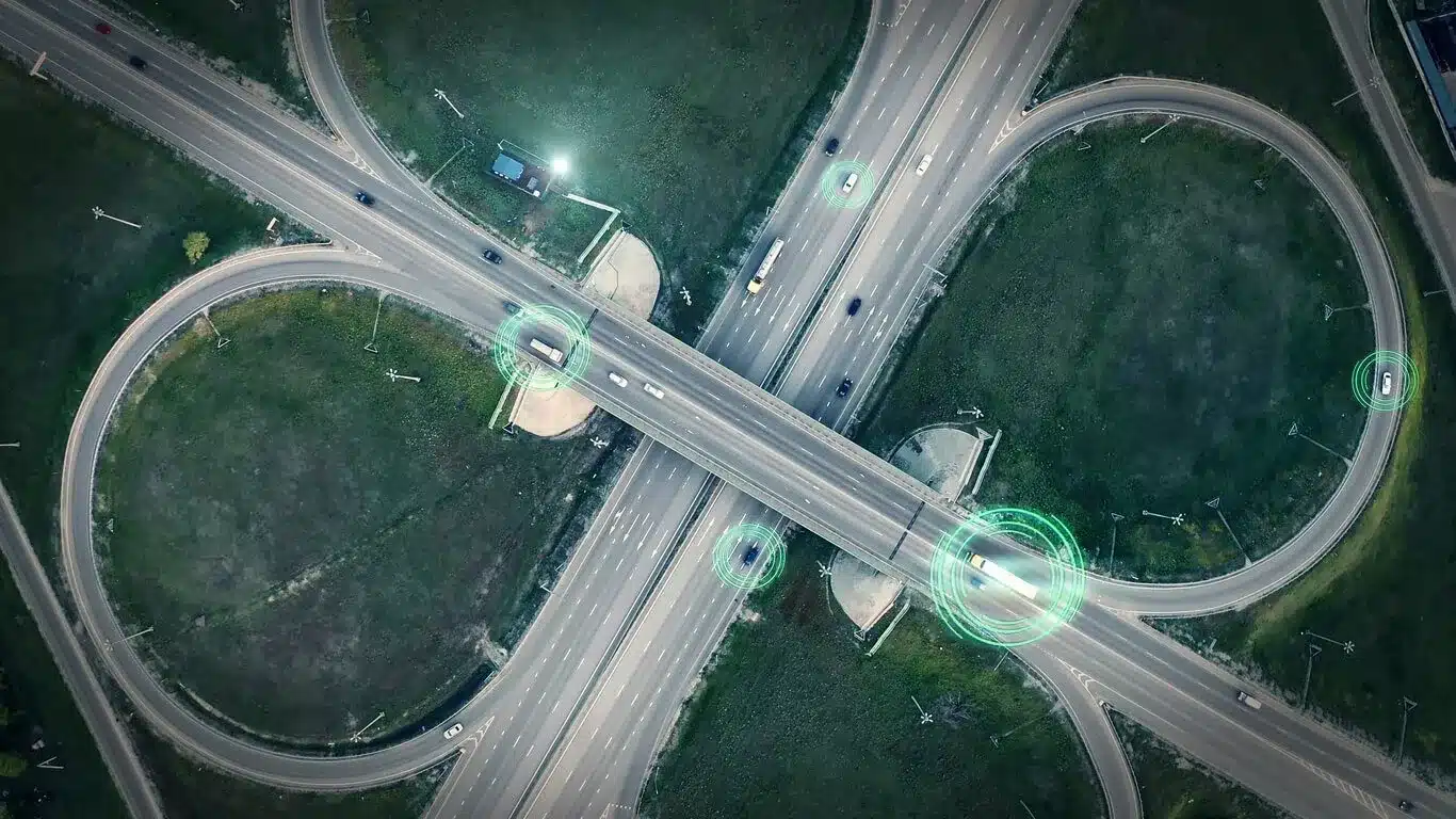 Luftaufnahme eines Autobahnkreuzes mit mehreren Fahrspuren und Schleifenauffahrten, markierte Fahrzeuge auf der Straße
